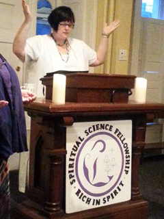 Rev. Eileen with her hands in the air in prayer behind a platform with a sign on it which says SSF