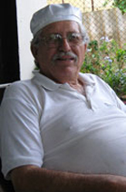 Sr. Jose Angel Pupo Olivarez, wearing a white hat and short sleeved shirt in a sitting position. He is looking towards the camera, he has white hair and is wearing a white hat.