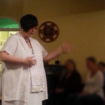 Eileen at an event working as a platform medium giving readings to people. she has short dark hair, is in white and wearing her minister stall.