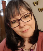 Image of Psychic Clairvoyant Medium, Eileen Casey Gonzalez. She has shoulder length dark hair, purple glasses and is wearing a pink sweater.